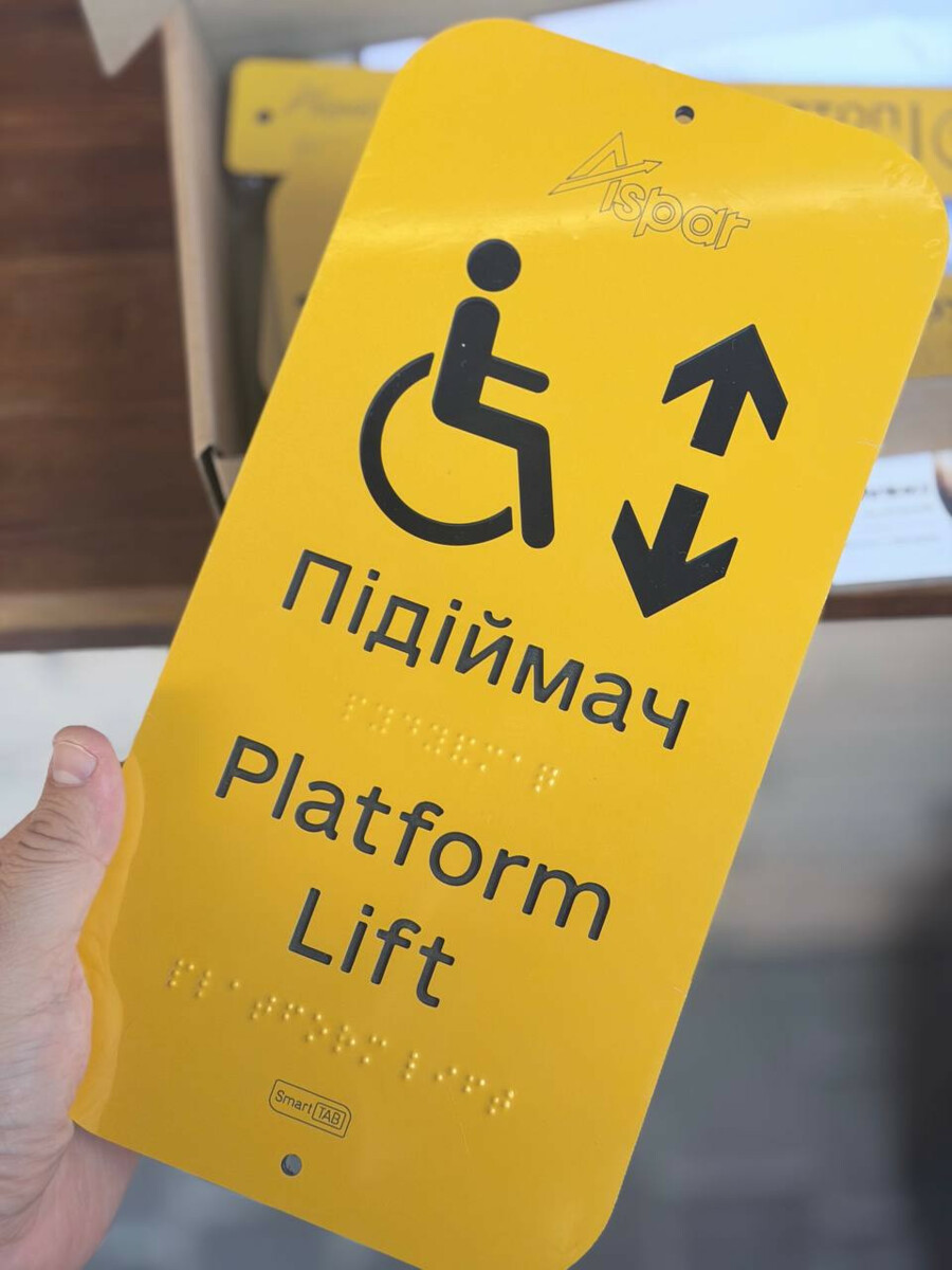 Жовта табличка ASPAR «Підіймач / Platform Lift» із символом крісла колісного, стрілками та рельєфними крапками